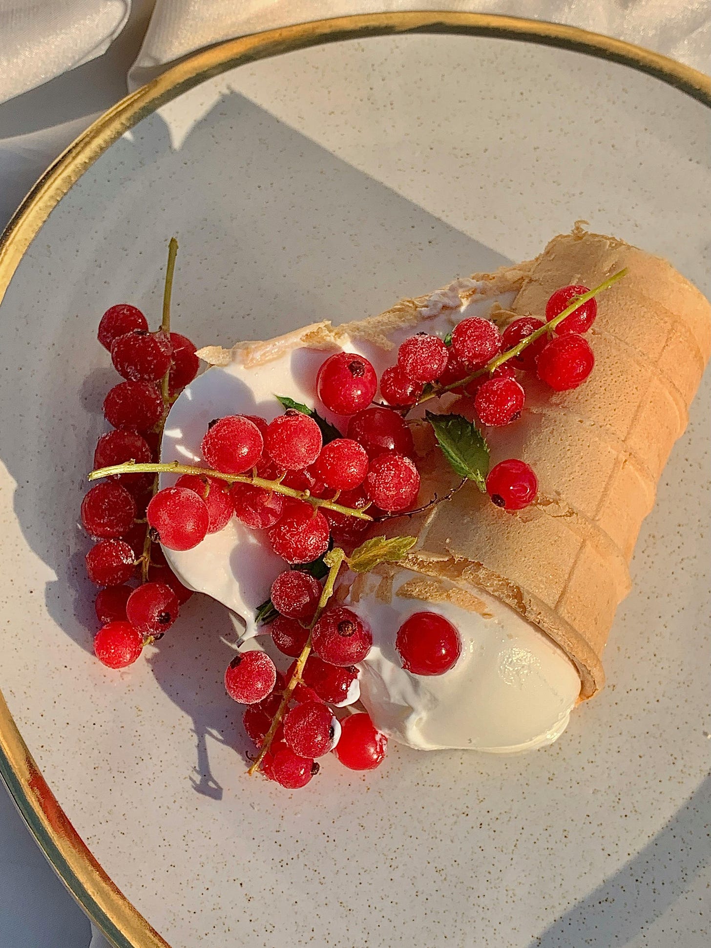 Vanilla ice cream cone broken in half on a plate with red currants on top
