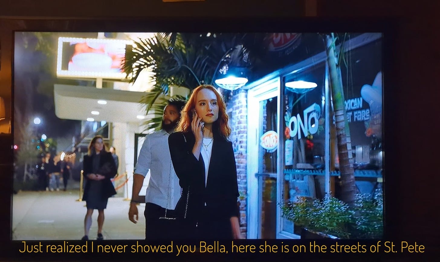 Bella, a thin white woman with long red hair, on the phone, captioned "Just realized I never showed you Bella, here she is on the streets of St. Pete"