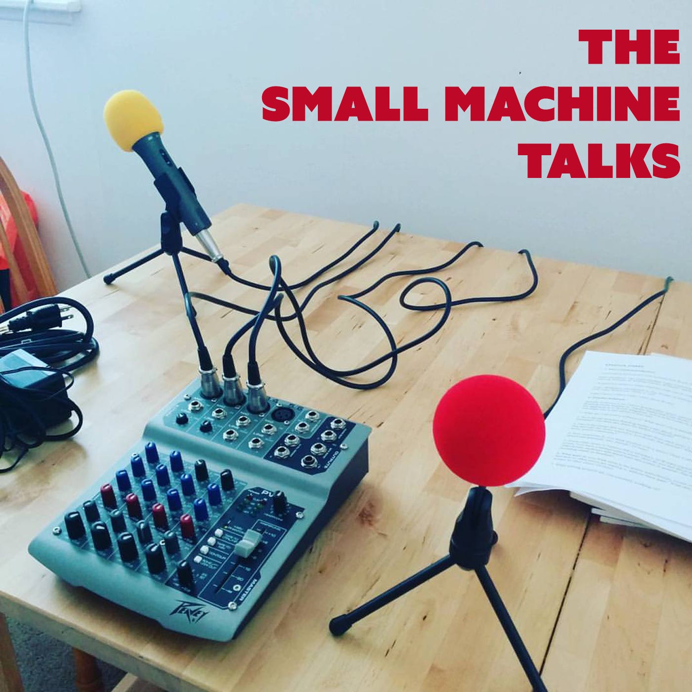 TEXT: THE SMALL MACHINE TALKS. IMAGE: microphones, sound equipment and papers on a wooden table