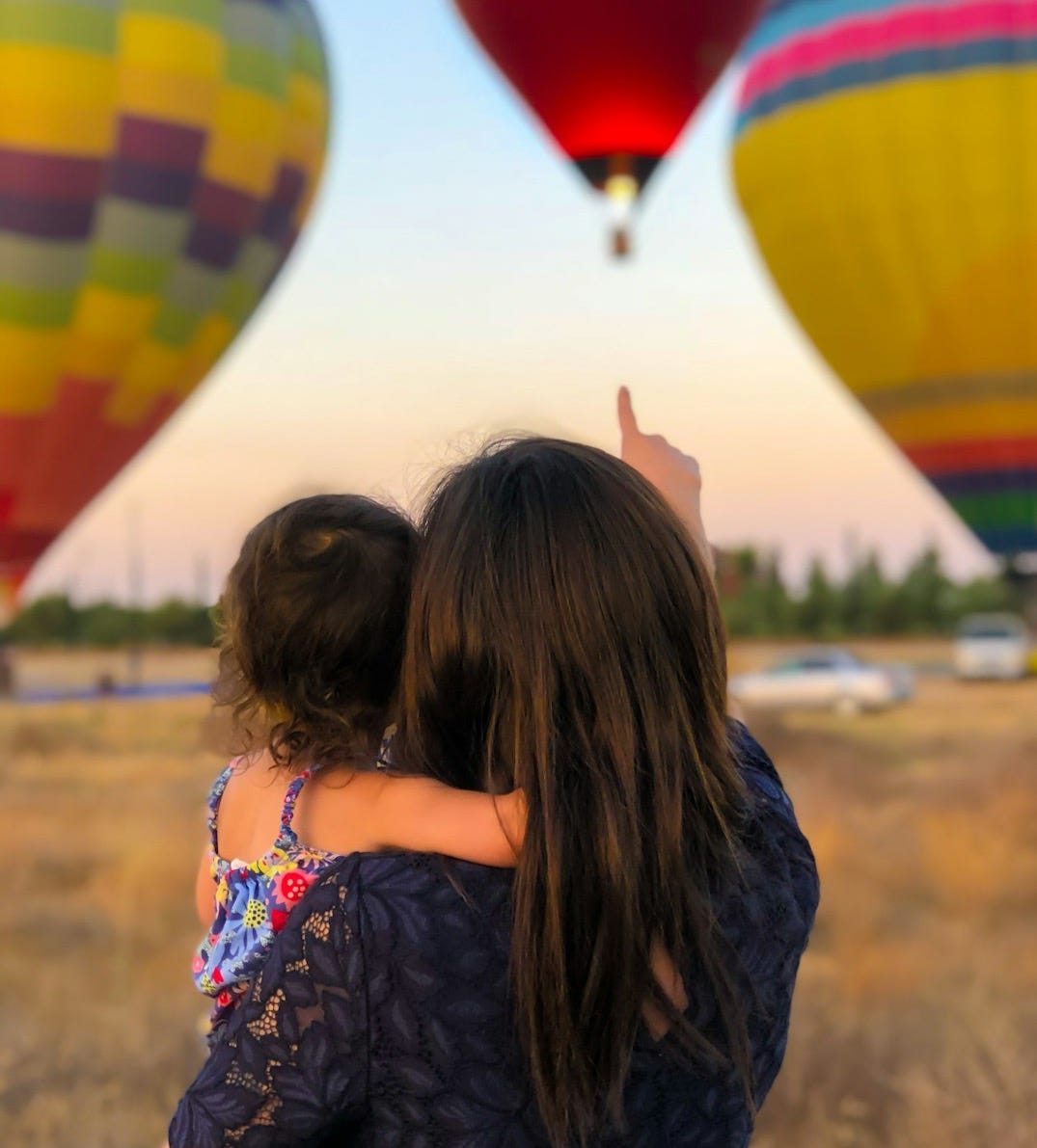 woman carrying toddler point at hot air balloon