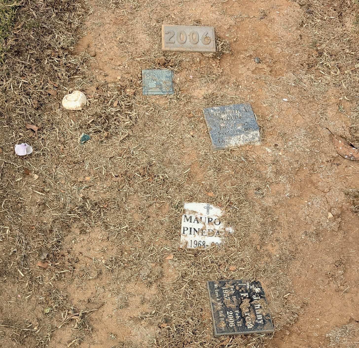 A grave marker reading 2006 has been joined by newer markers identifying individuals within the mass grave. The name "Mauro Pineda" is legible on one of the markers