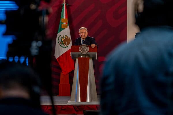 Mexico’s president, Andrés Manuel López Obrador, stands at a podium with the Mexican flag on display behind him.