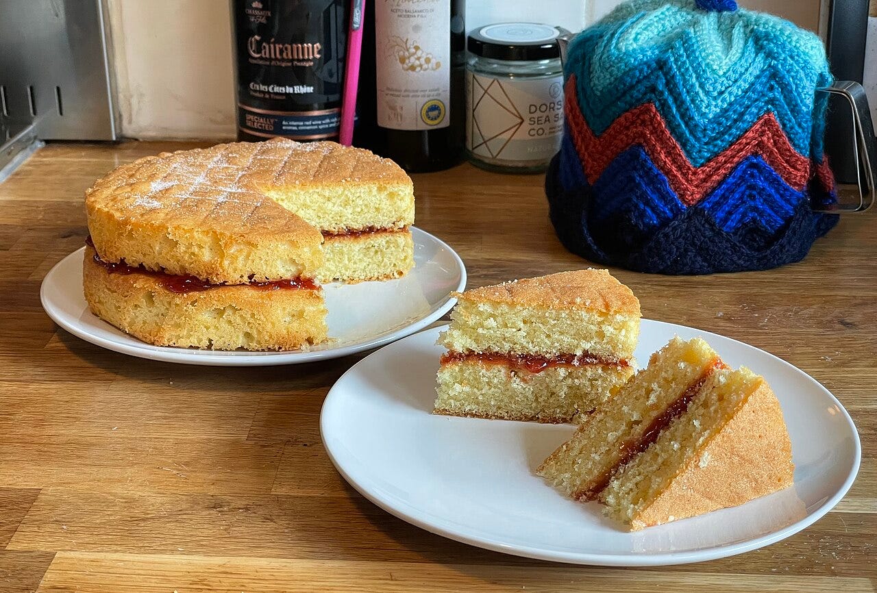 Two tier Victoria sandwich cake with a filling of strawberry jam; two slices have been taken ready to serve, and demonstrate the cake's construction