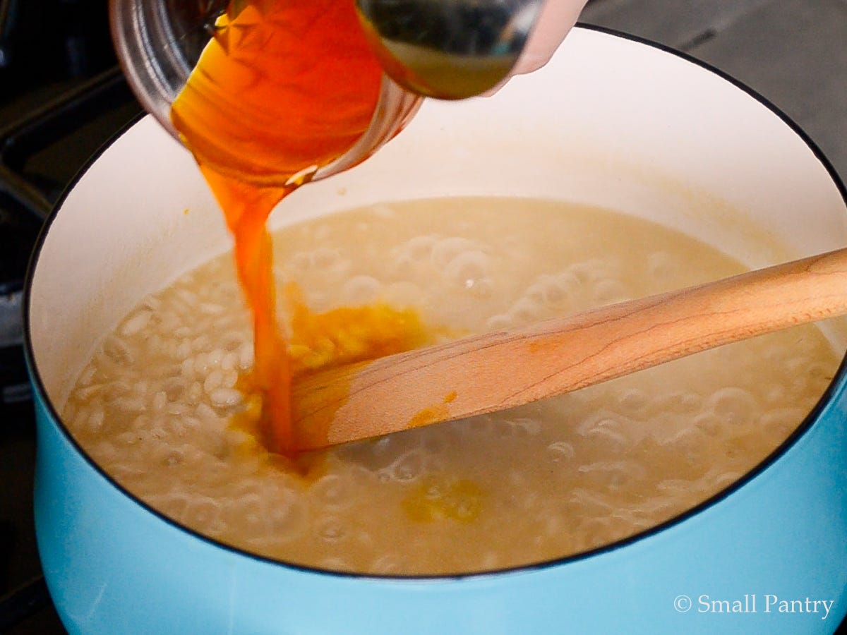 Saffron steeped in warm broth being poured into partially cooked risotto