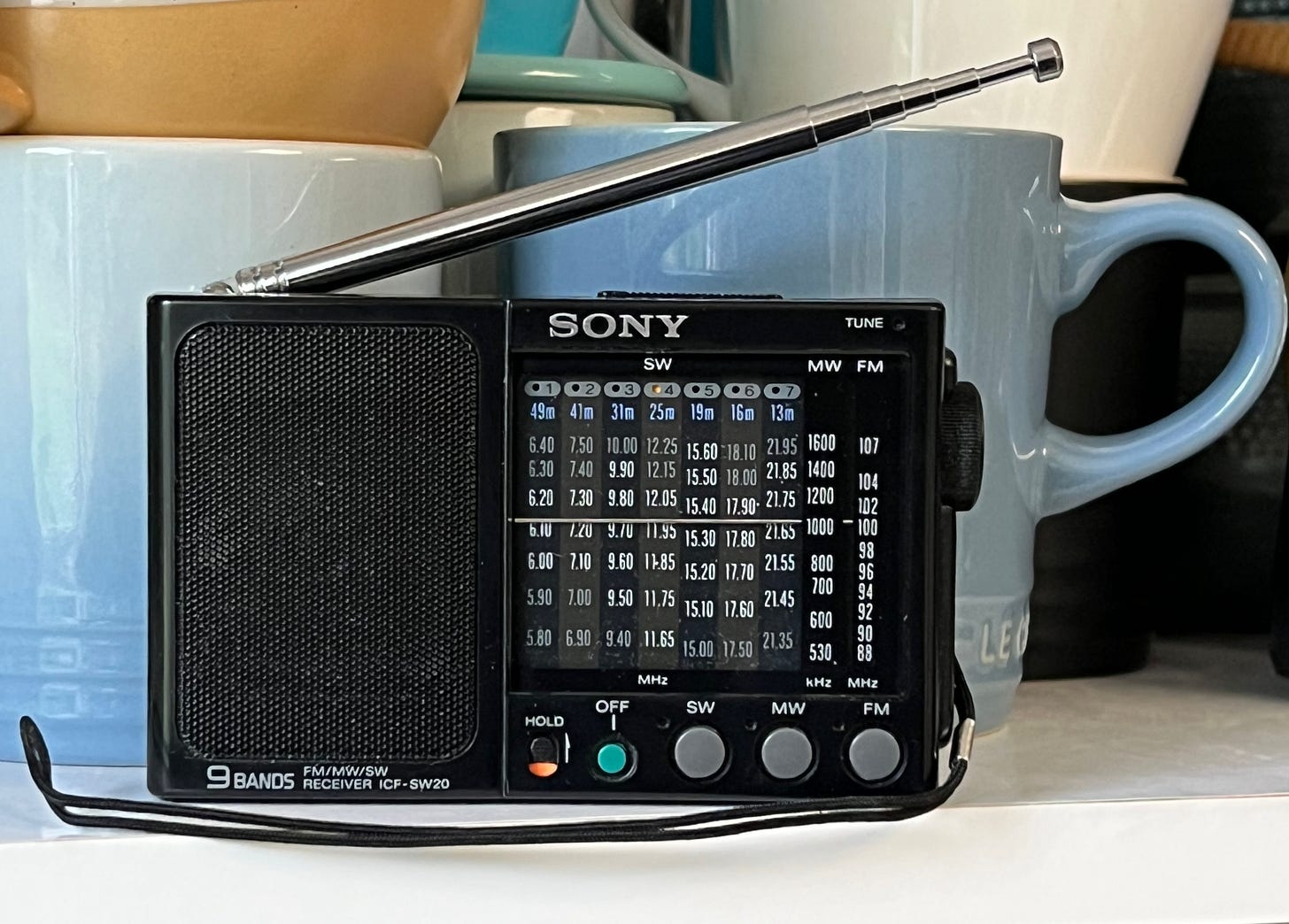 A small shortwave radio site on a shelf with some cups and mugs