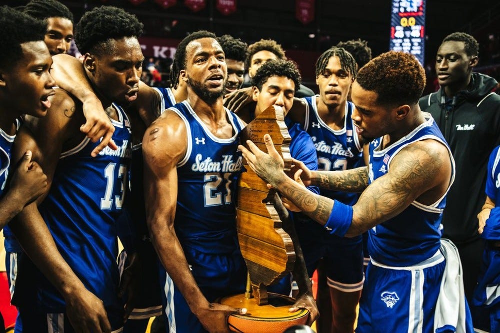 Al-Amir Dawes (foreground, right) looks at the Garden State Hardwood Classic trophy as his Seton Hall teammates celebrate defeating Rutgers on Dec. 11, 2022. (Photo by Lokesh Sutherland / courtesy of Seton Hall athletics)