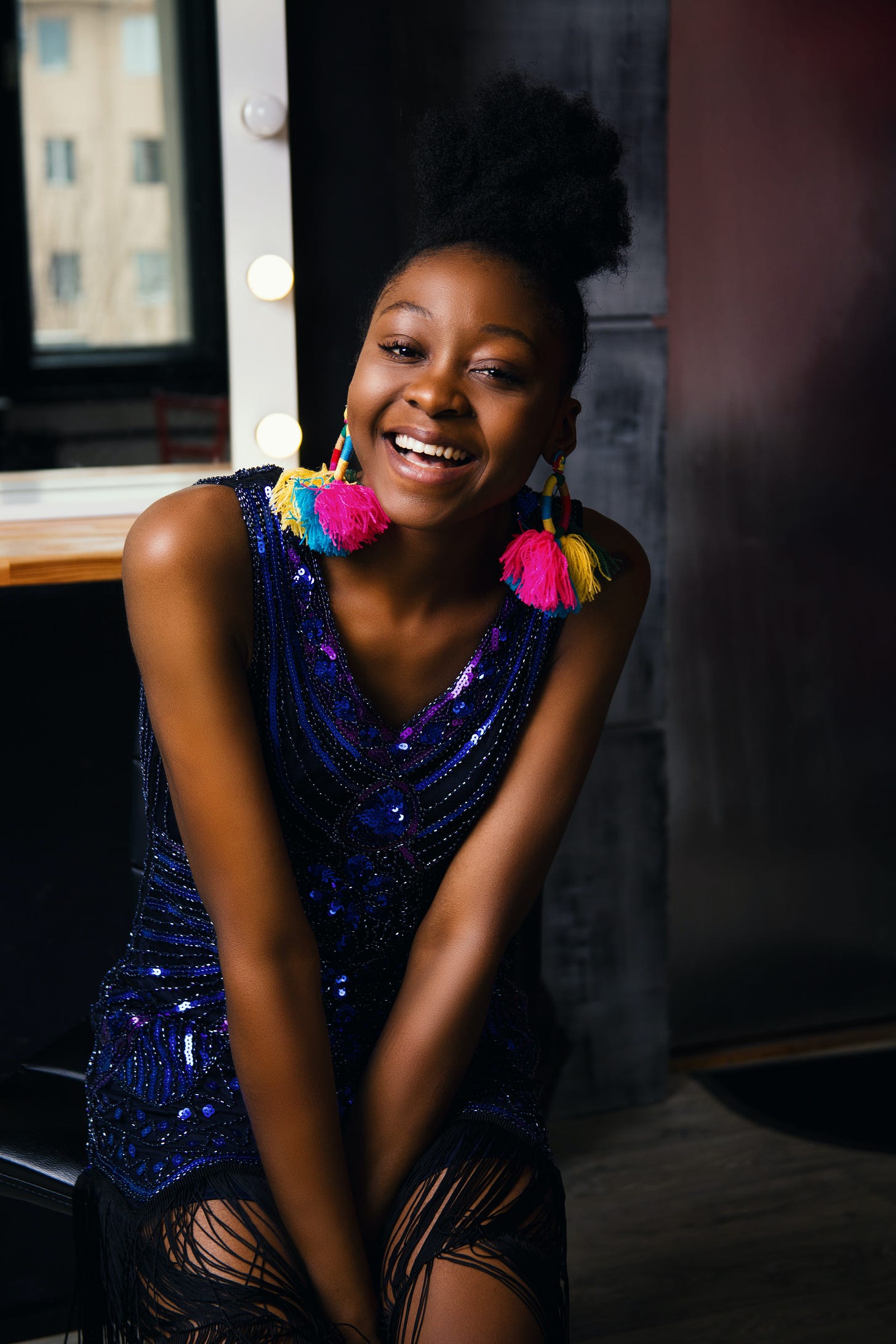 A woman in a purple sequined dress with colorful earrings, smiling