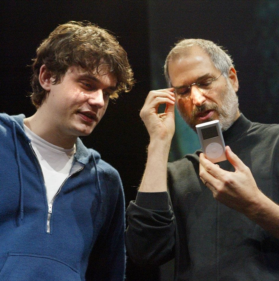 Apple CEO Steve Jobs (R) looks at a new iPod mini with recording artist John Mayer at the Macworld expo January 6, 2004 in San Francisco. Jobs announced several new products including the new iLife 4 software and the 4 GB iPod mini which comes in four different colors. 