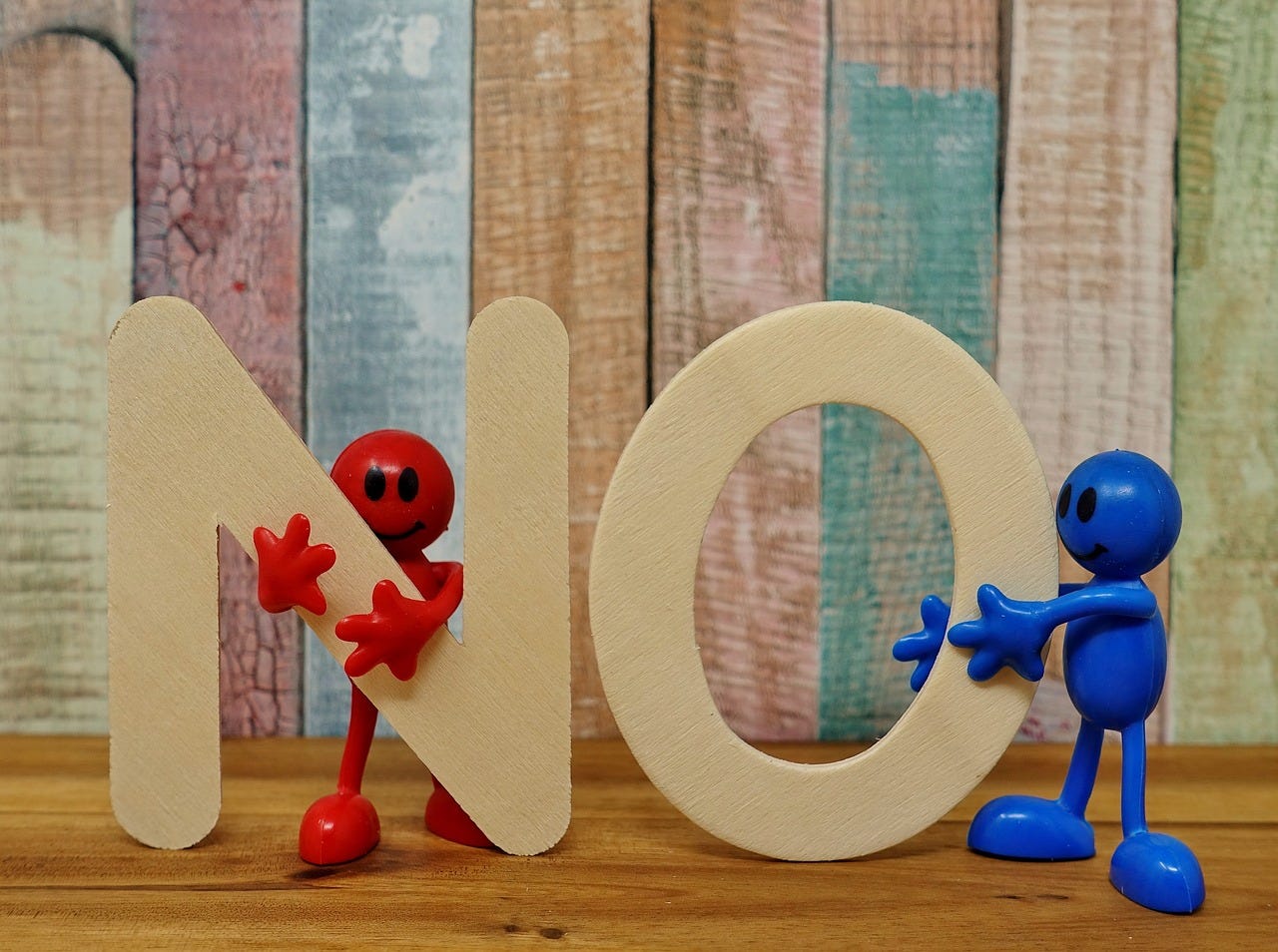 Against the background of a fence panel, two figurines (one blue, one red) hold up the letters "N" and "O"