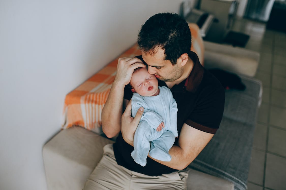 Free From above of tender father with adorable sleeping little baby in arms sitting on comfortable couch in light room during bedtime Stock Photo