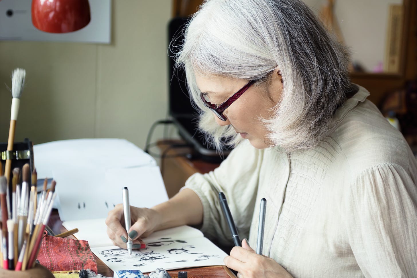 An older Asian woman drawing at a desk.