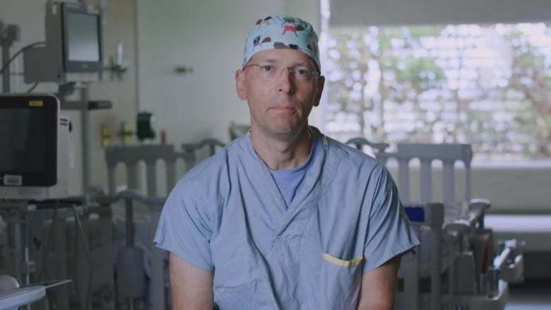 Dr. Paul Moxham is pictured in scrubs and a colourful surgeon's cap in a hospital setting. 