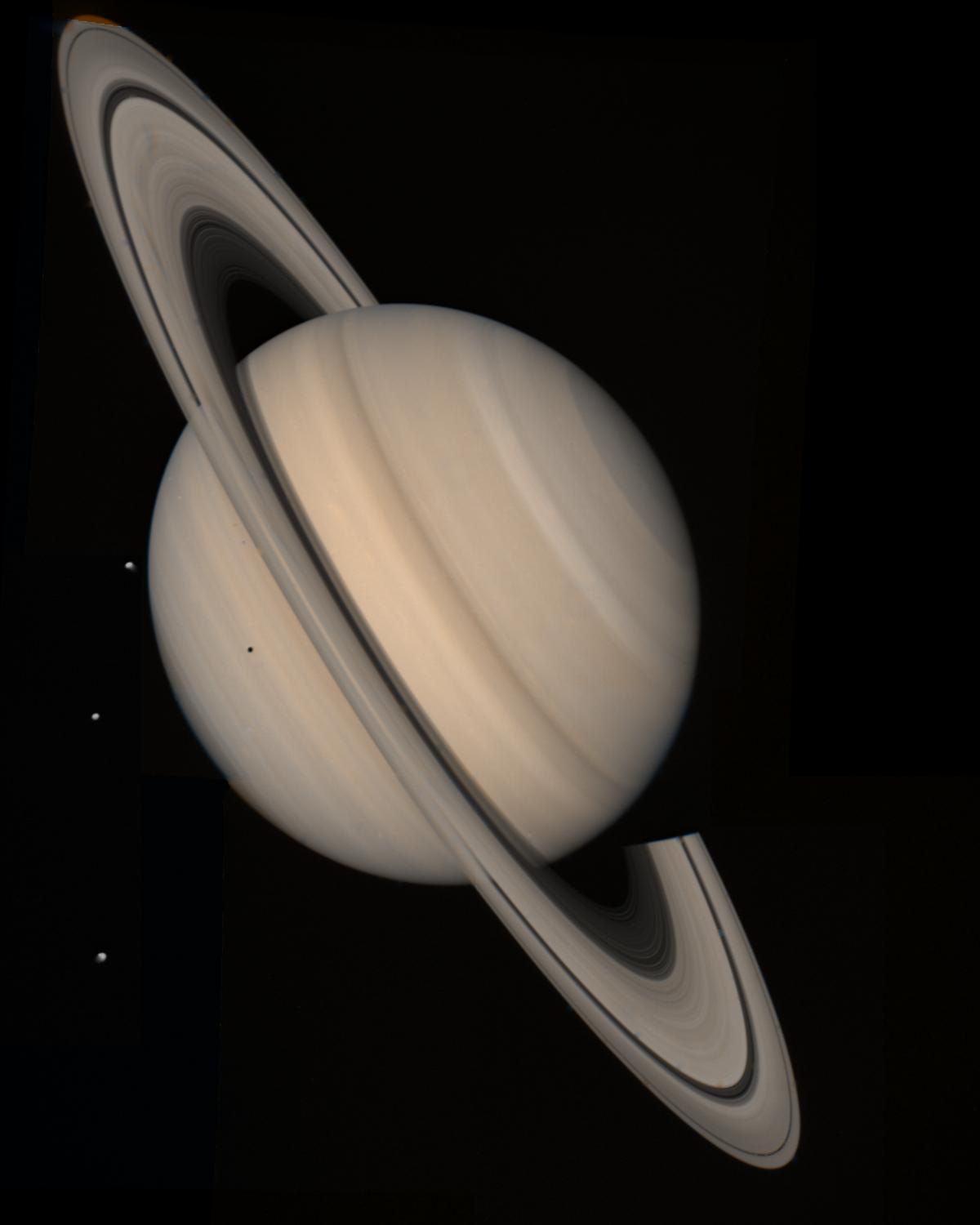 The planet Saturn is a striped beige orb, surrounded by beige and black rings, against the dark black of space. 