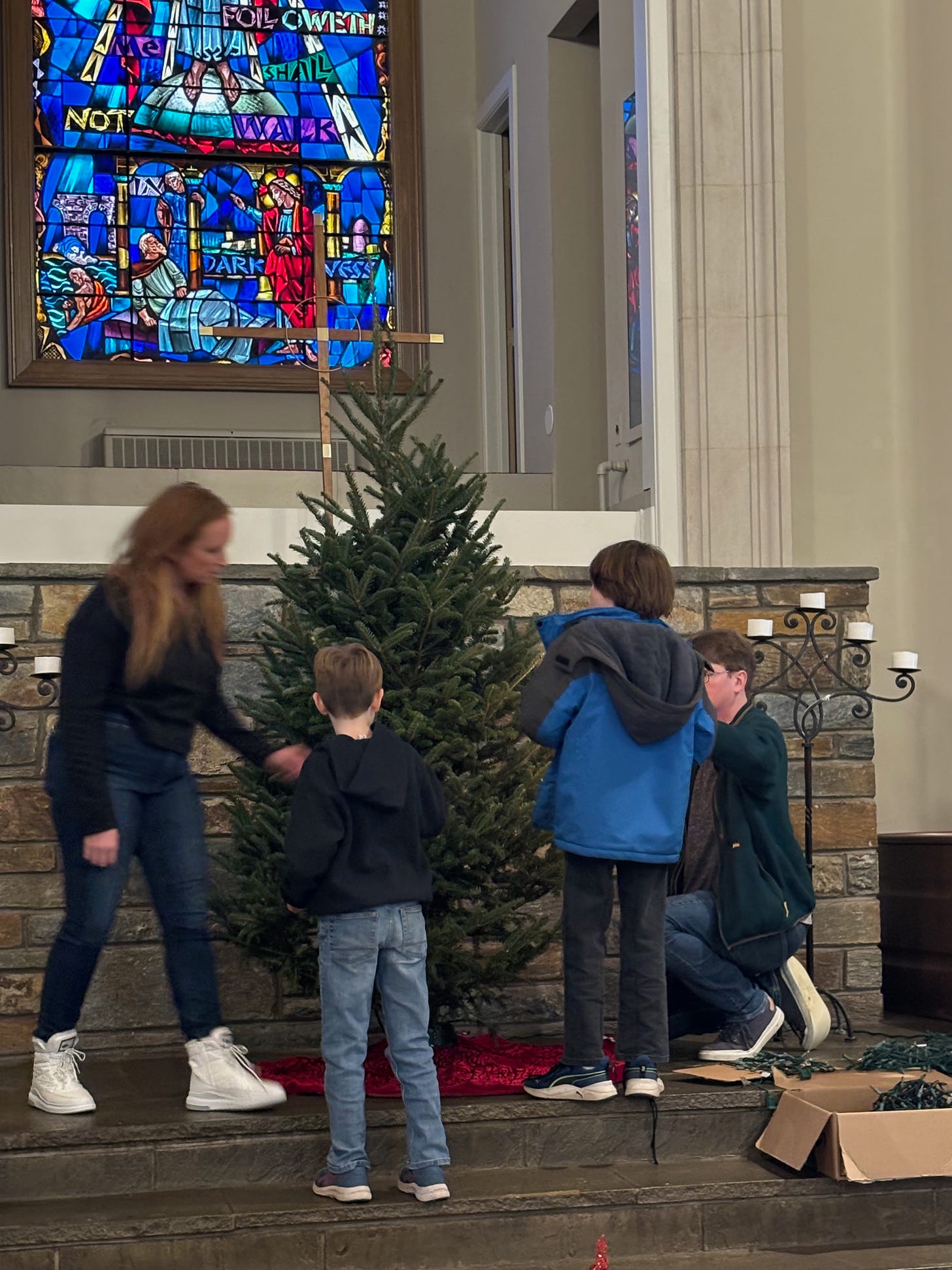 My two sons and my husband (all of whom are white) with another member of our church standing in front of an undecorated Christmas tree, with a cross and stained glass behind it
