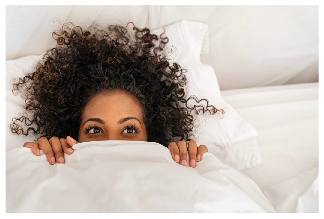 Curly haired woman peeks out from under a white duvet cover