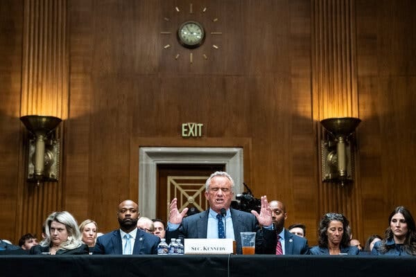 Robert F. Kennedy Jr. gestures with both hands as he speaks from behind a table in a Senate hearing room.