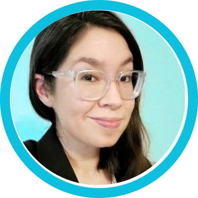 A headshot portrait of Angela wearing clear acrylic glasses and a black suit jacket