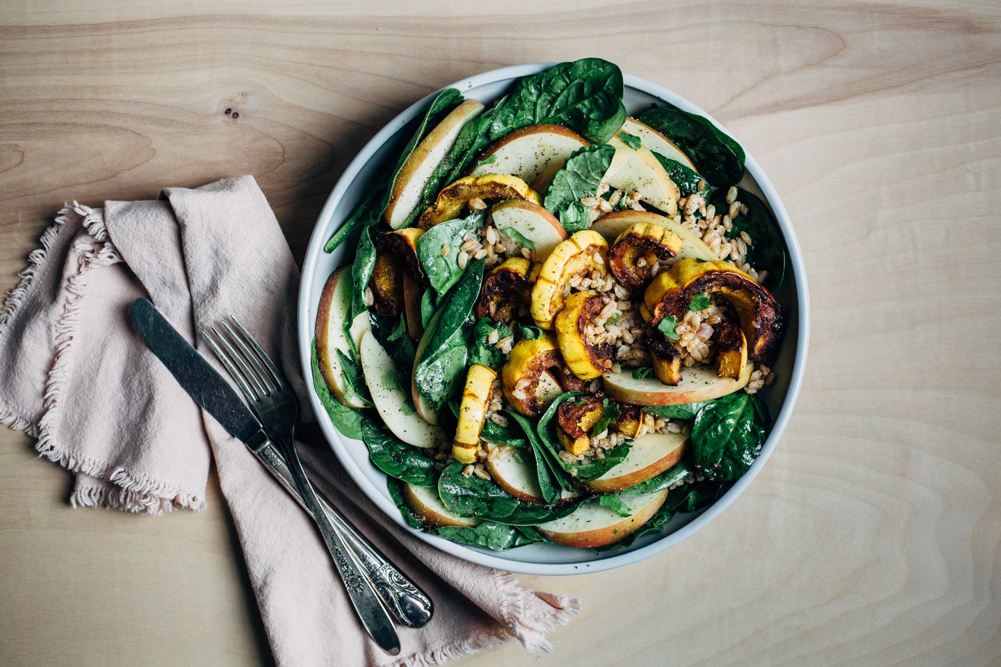 A salad bowl filled with greens, farro, apples, and roasted squash
