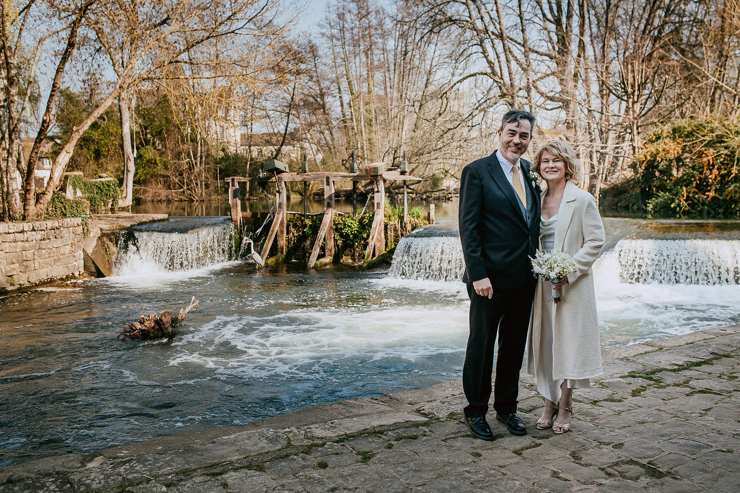 A man and a woman pose for wedding portraits in front of a waterfall in France