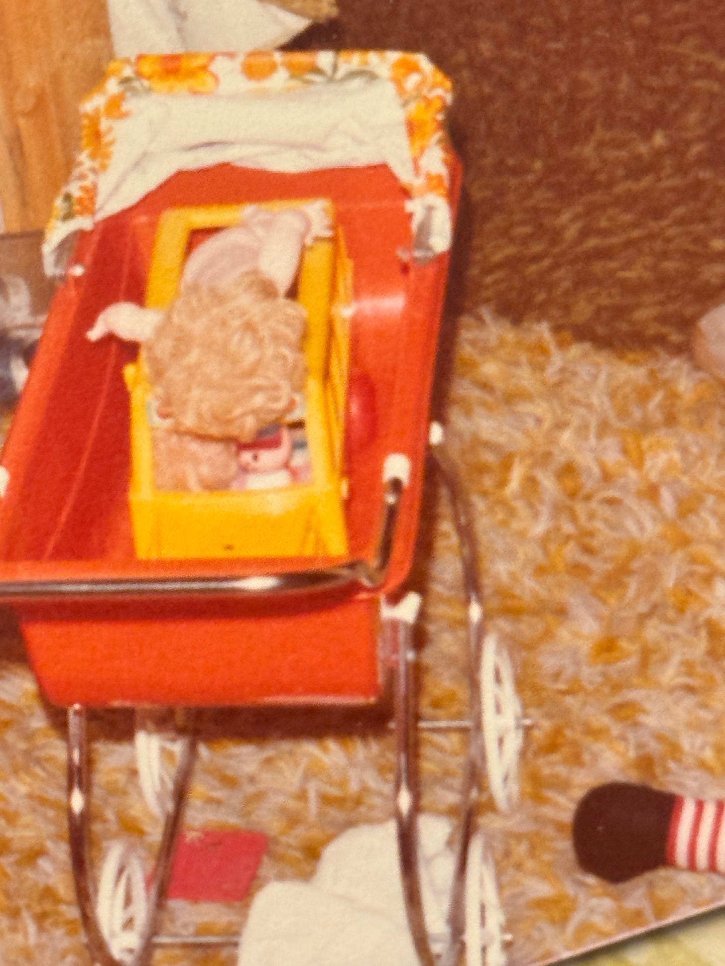 zoomed in image of a 1970s orange plastic stroller with a small yellow schoolbus inside holding a plastic baby doll