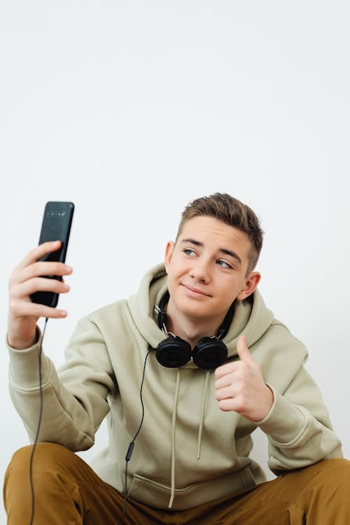 Free Teenage Boy Showing Thumbs Up Gesture to his Smart Phone  Stock Photo