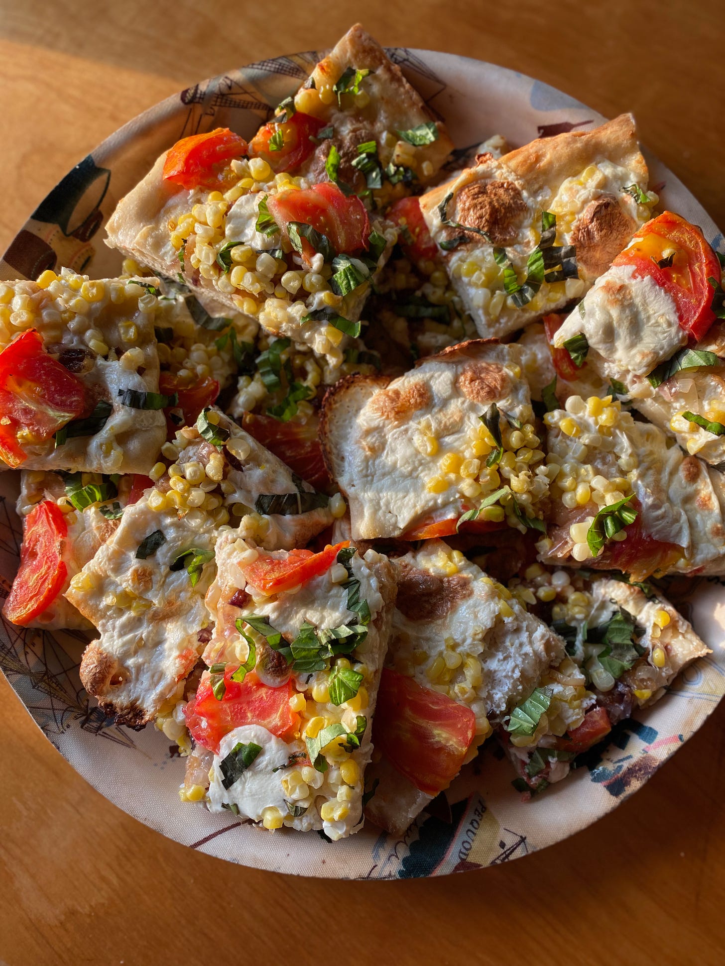 A plate of rectangular slices of pizza, topped with corn, tomatoes, and basil, in the evening sun.