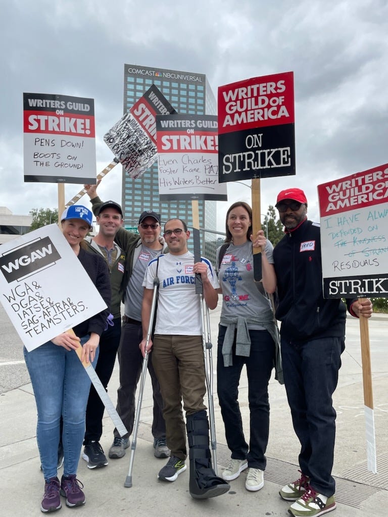 A group of veterans and writers holding "Writers Guild of America on Strike" signs in front of the Comcast/NBC Universal building in Studio City.