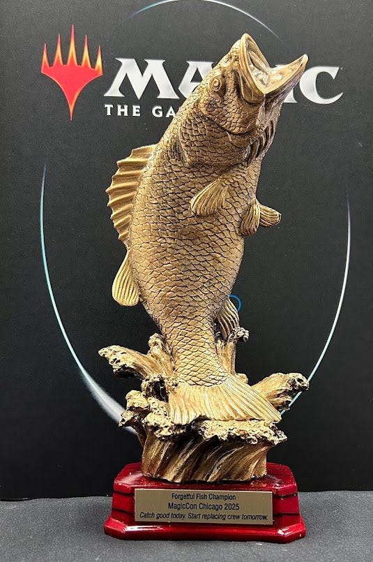 A 12" bronze trophy of a bass splashing out of the water. A plaque reads "Forgetful Fish Champion - MagicCon Chicago 2025. "Catch good today. Start replacing crew tomorrow"