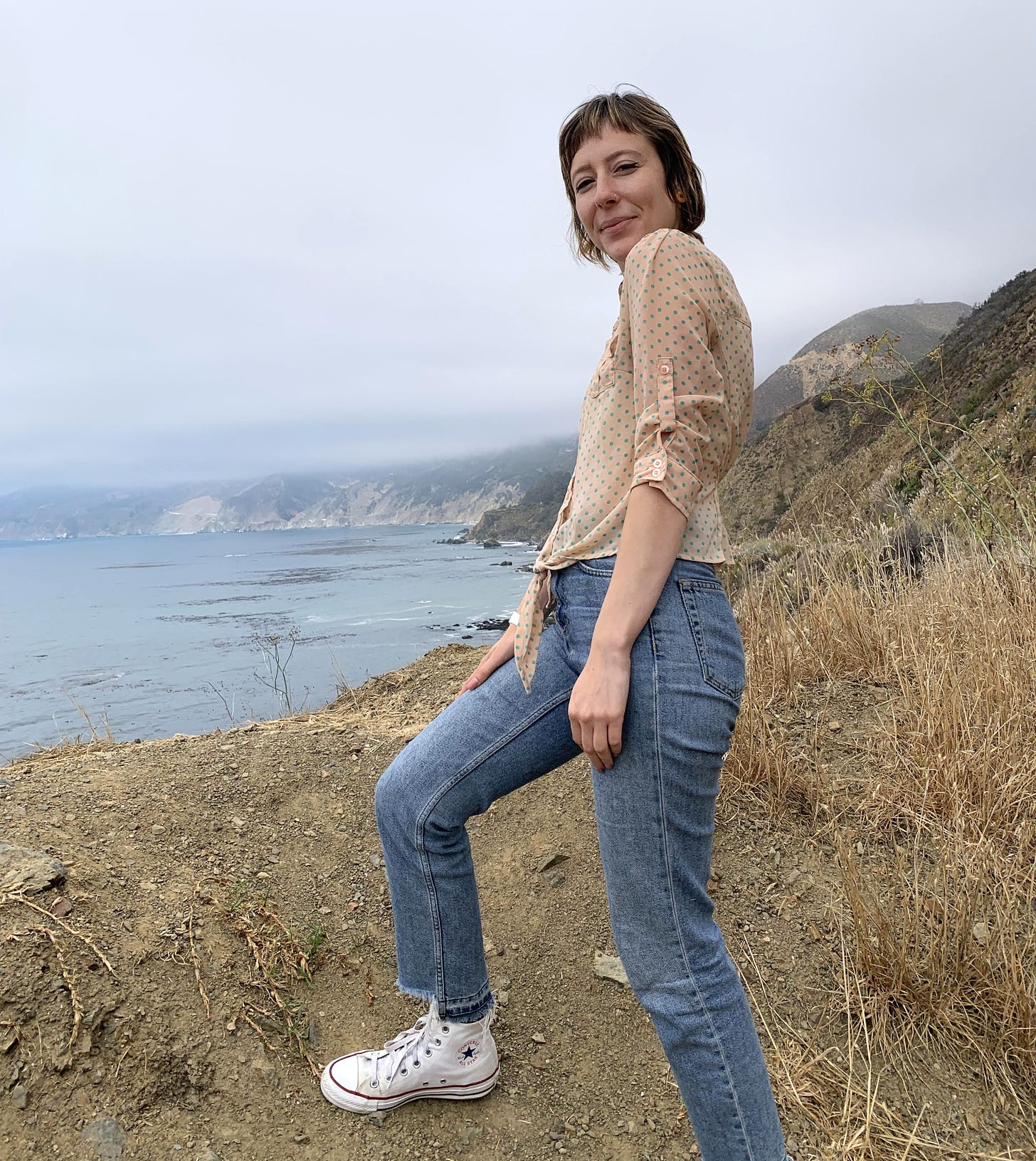 Me in a polka dot shirt, jeans, and Converse overlooking the Pacific Ocean in Big Sur