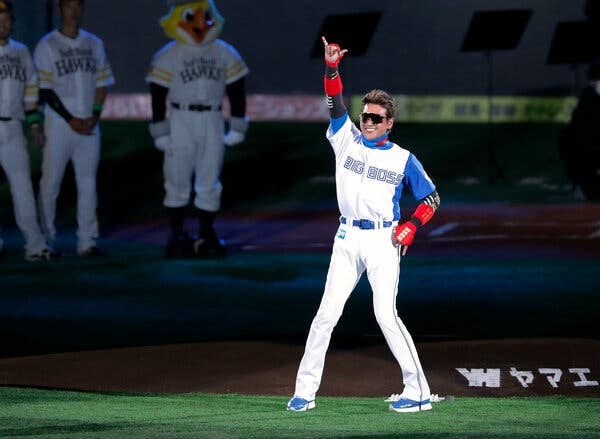 Tsuyoshi Shinjo, wearing a Nippon Ham Fighters uniform with "Big Boss" written across the chest, gestures toward fans while standing in a spotlight.