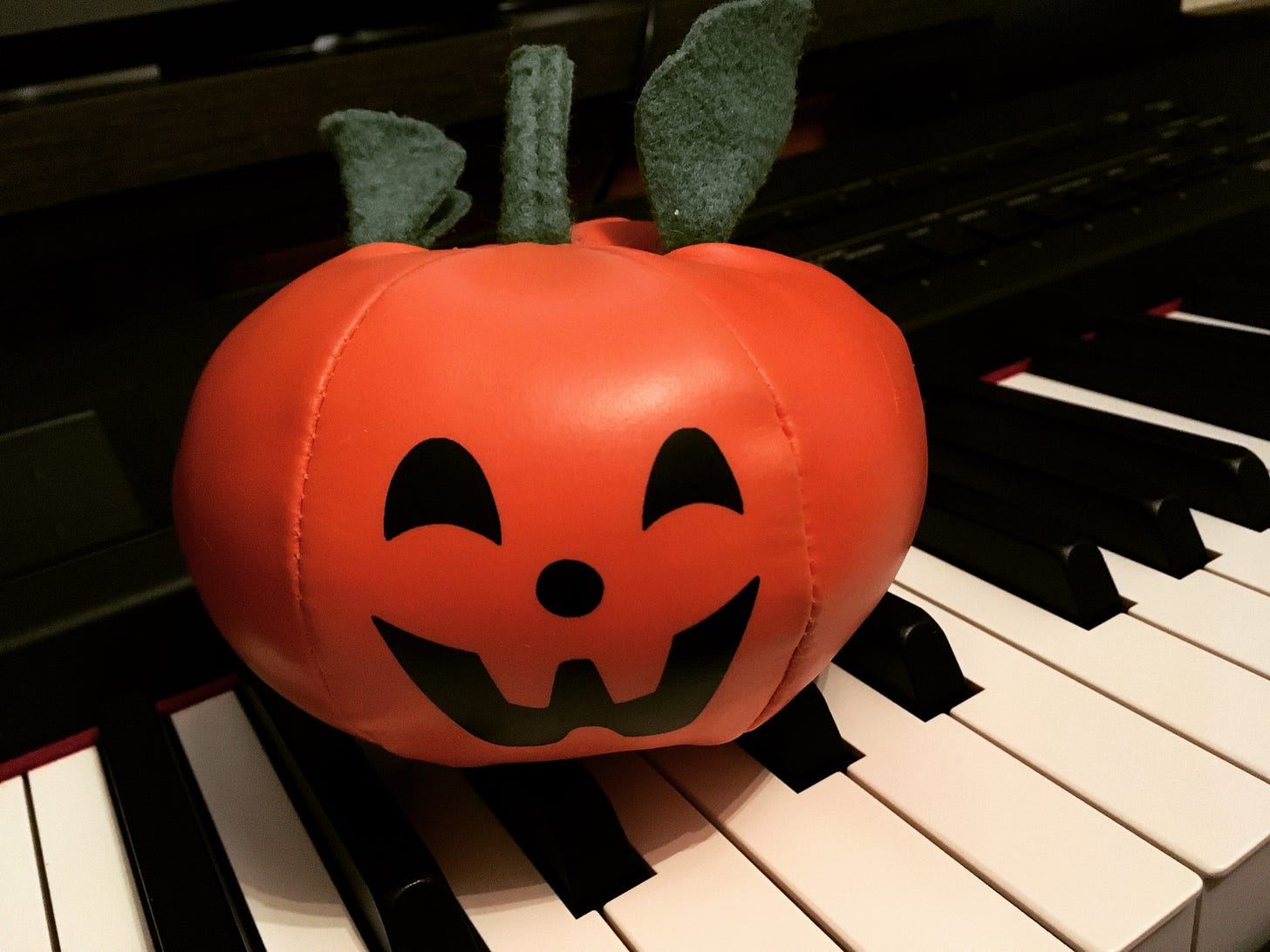 A little plush jack-o'-lantern sitting on top of a piano keyboard.
