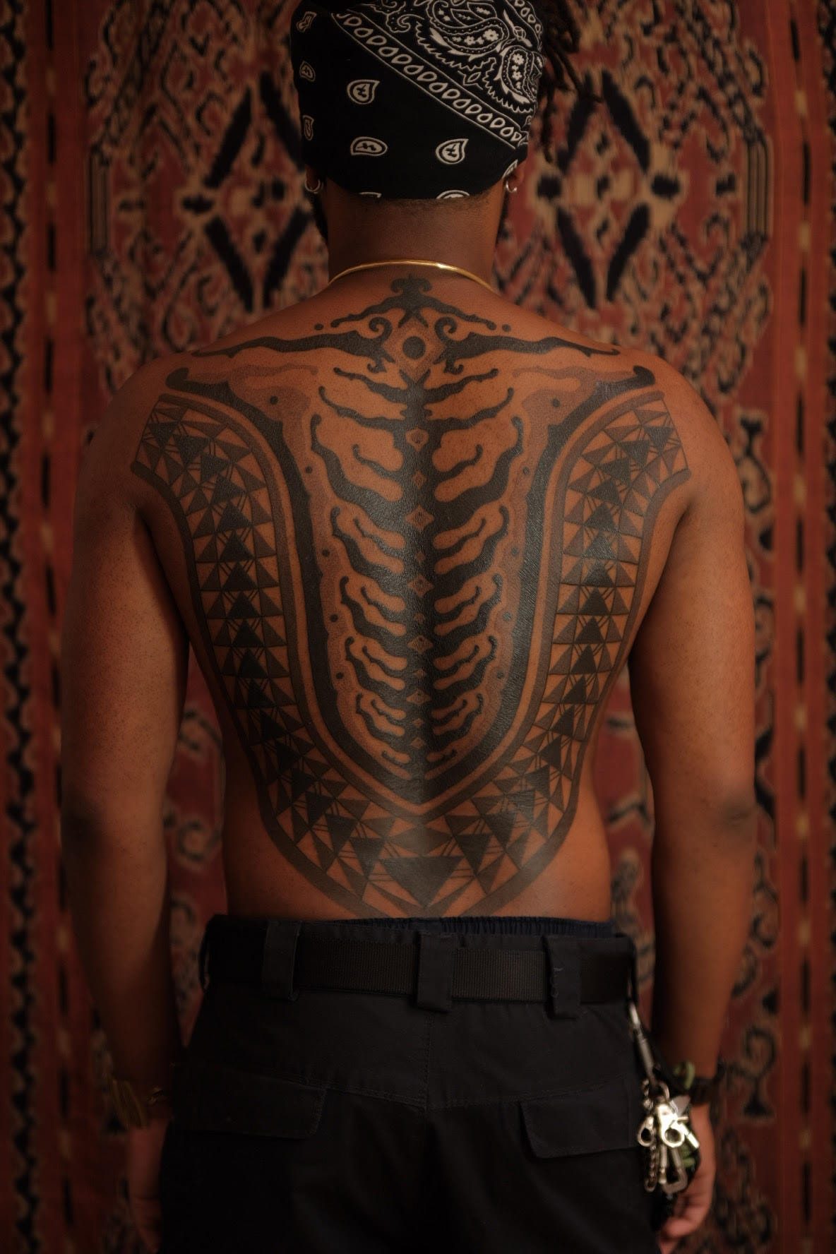 brown skin man with large tribal tattoo descending from his nape to his backside area