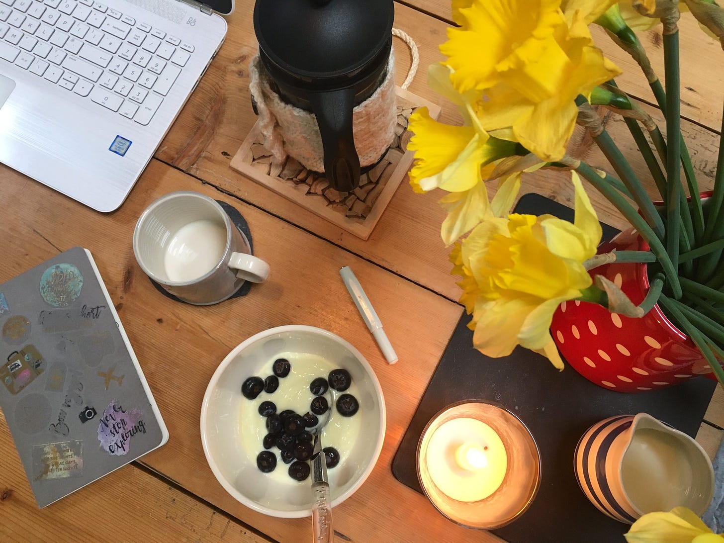 Notebook and laptop on a kitchen table from above, with coffee, breakfast and a candle