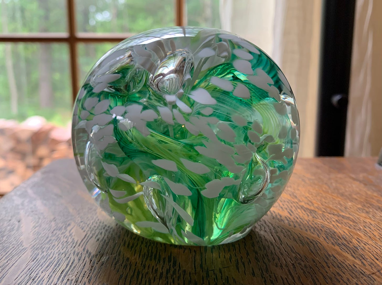 A handblown glass sphere with swirls of green, yellow, and white running through it.