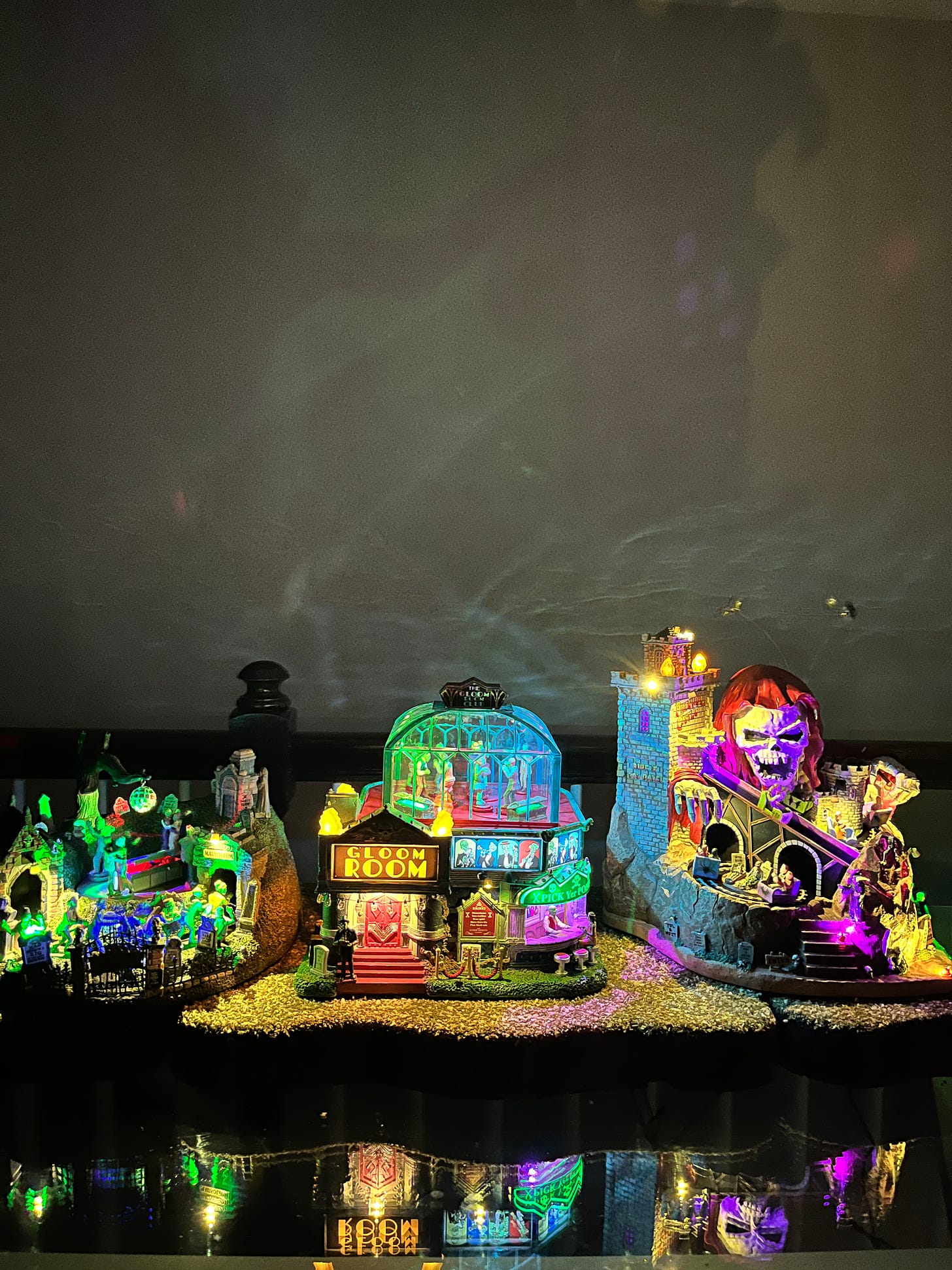 The SpookyTown Graveyard, Gloom Room, and Phantom Castle cast backlight on the wall. The glass tabletop reflects the structures, gives the illusion of a waterfront setting. 