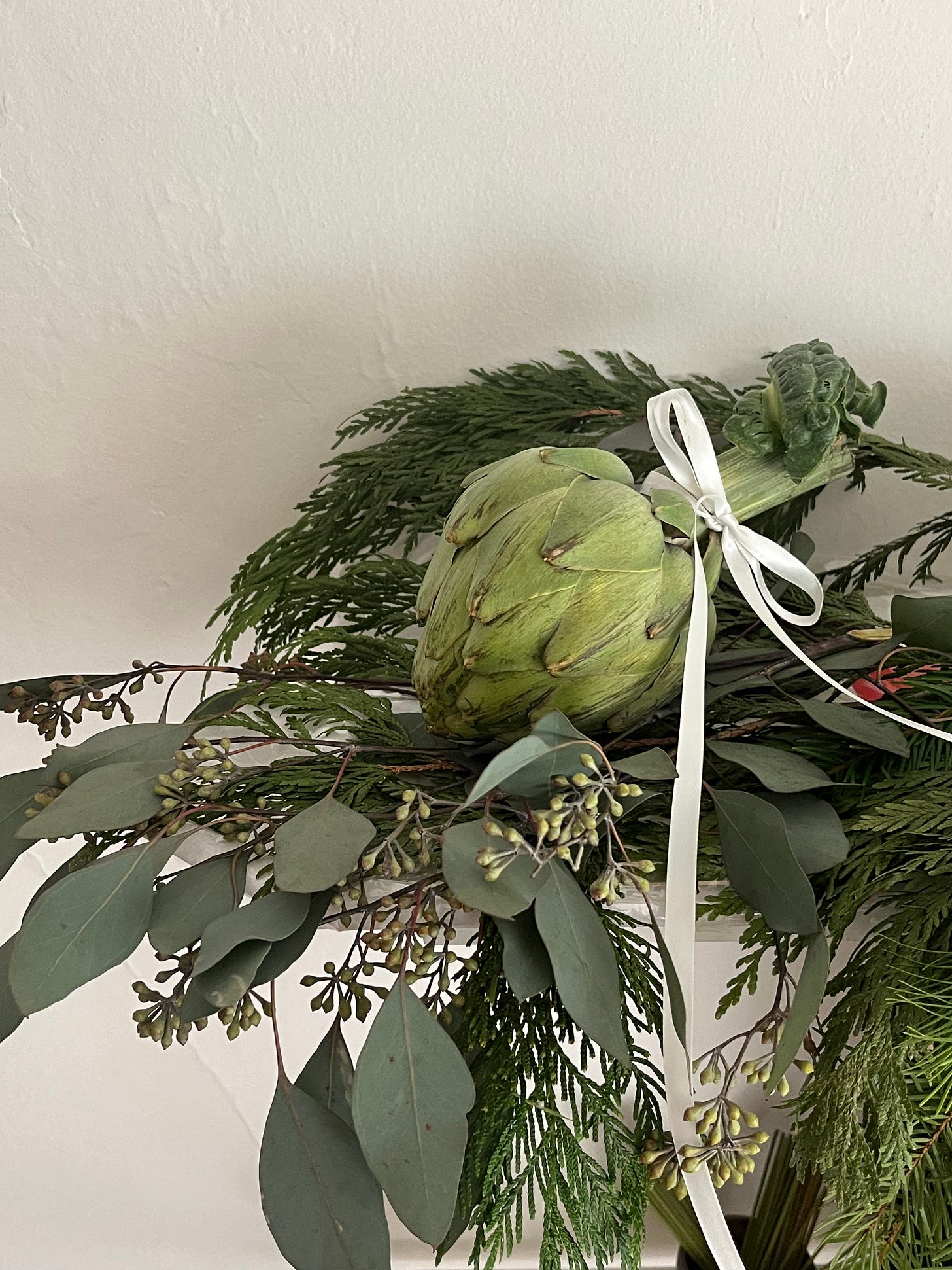 Mantle covered in garland, eucalyptus, and head of artichoke tied with a bow.