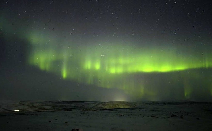 A green aurora in a starry sky, above a snowy landscape