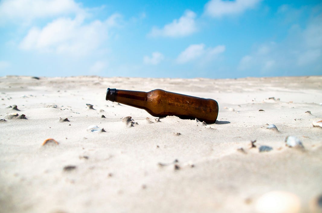 Empty brown bottle on beach with blue sky in background