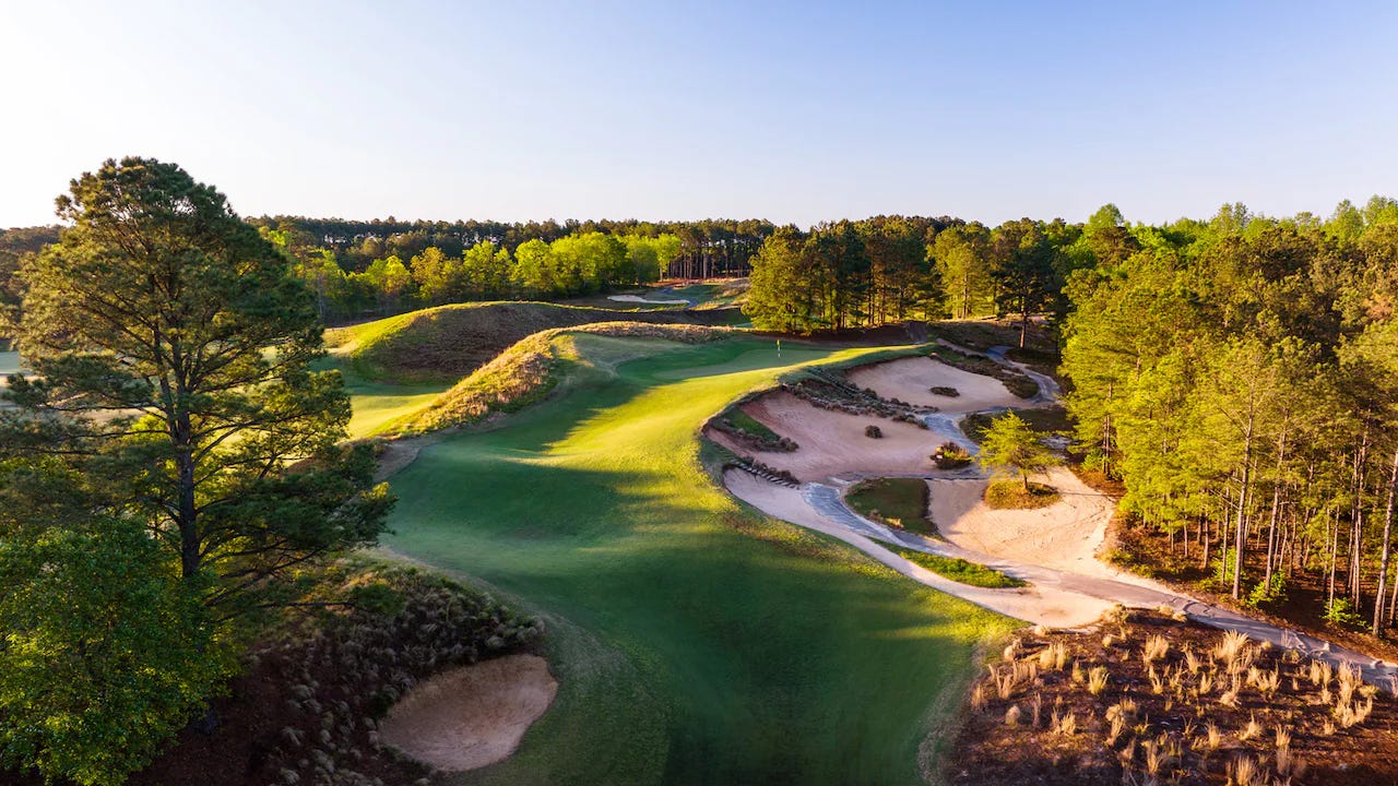 Aerial view of a golf hole at Tobacco Road featuring dramatic sand waste areas, undulating green fairways, and pine forest surroundings. The late afternoon sunlight creates striking shadows across the sculptured terrain and bunkers. Aerial view of a golf hole at Tobacco Road featuring dramatic sand waste areas, undulating green fairways, and pine forest surroundings. The late afternoon sunlight creates striking shadows across the sculptured terrain and bunkers.