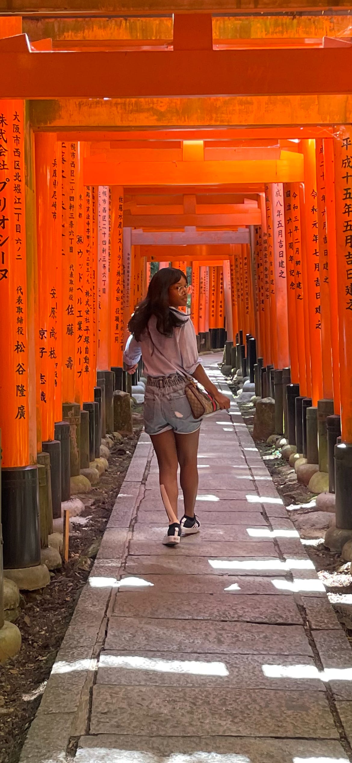  Kat Lewis, a Black woman, walking through the orange torii gates of Fushimi Inari Taisha.