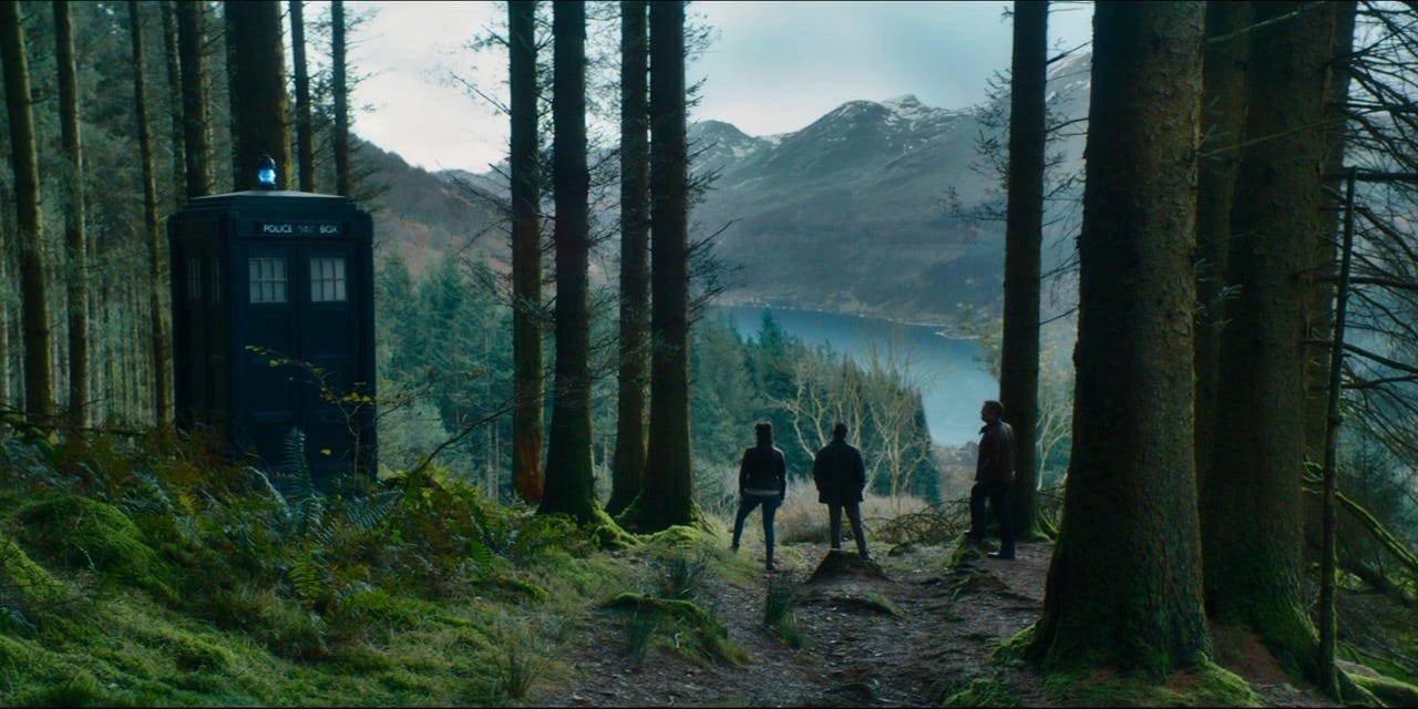 This image shows the TARDIS sitting in a beautiful forest that opens onto a gorgeous Norwegian fjord in "It Takes You Away" (Doctor Who Series 11's ninth episode). With their backs to camera (and from left to right), Yasmin "Yaz" Khan (played by Mandip Gill), Graham O'Brien (played by Bradley Walsh), and Ryan Sinclair (played by Tosin Cole) stand on a forest trail while gazing at the fjord. This image shows the TARDIS sitting in a beautiful forest that opens onto a gorgeous Norwegian fjord in "It Takes You Away" (Doctor Who Series 11's ninth episode). With their backs to camera (and from left to right), Yasmin "Yaz" Khan (played by Mandip Gill), Graham O'Brien (played by Bradley Walsh), and Ryan Sinclair (played by Tosin Cole) stand on a forest trail while gazing at the fjord.