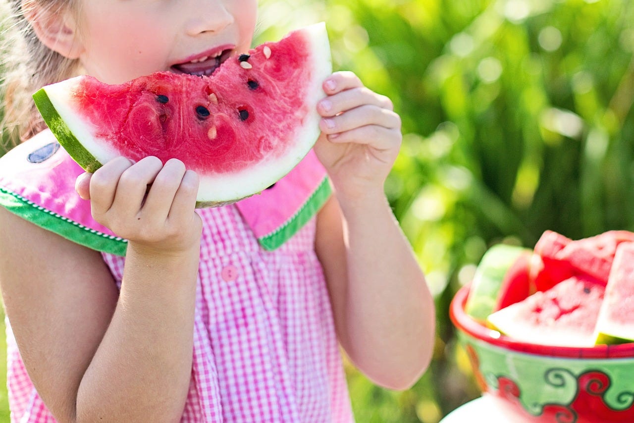 a child holds a slice of watermelon, ready to take a bite