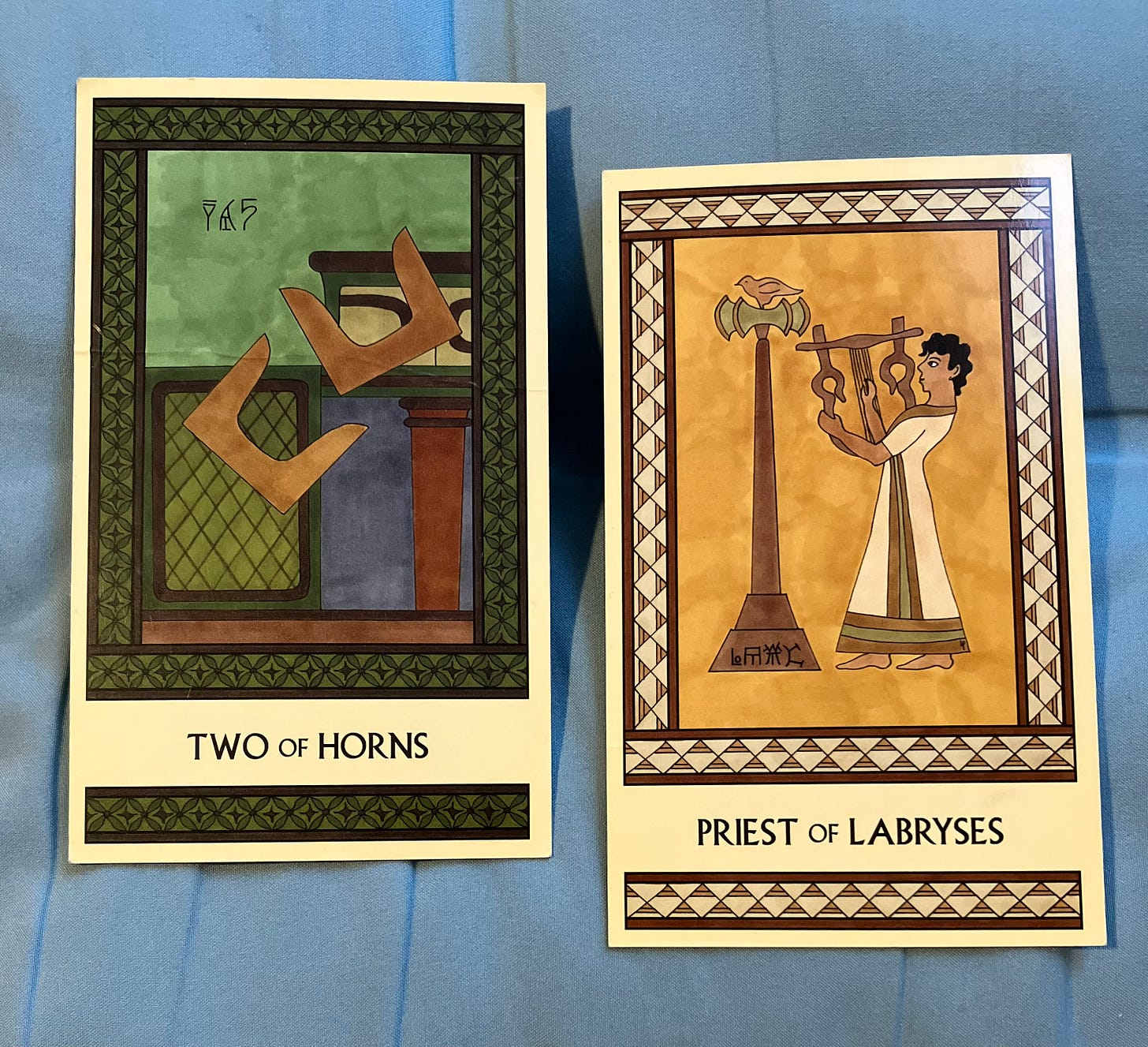 Two Minoan Tarot cards side by side on a grayish-blue background. The Two of Horns is in shades of green and brown and shows two pairs of Minoan sacred horns tumbling off a shrine. The Priest of Labryses is in shades of gold, cream, and tan and shows a Minoan man in a long robe, facing left, playing a lyre in front of a tall labrys.