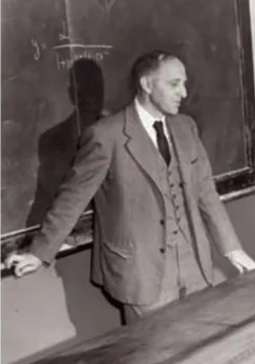 A person in a suit standing in front of a chalkboard

Description automatically generated