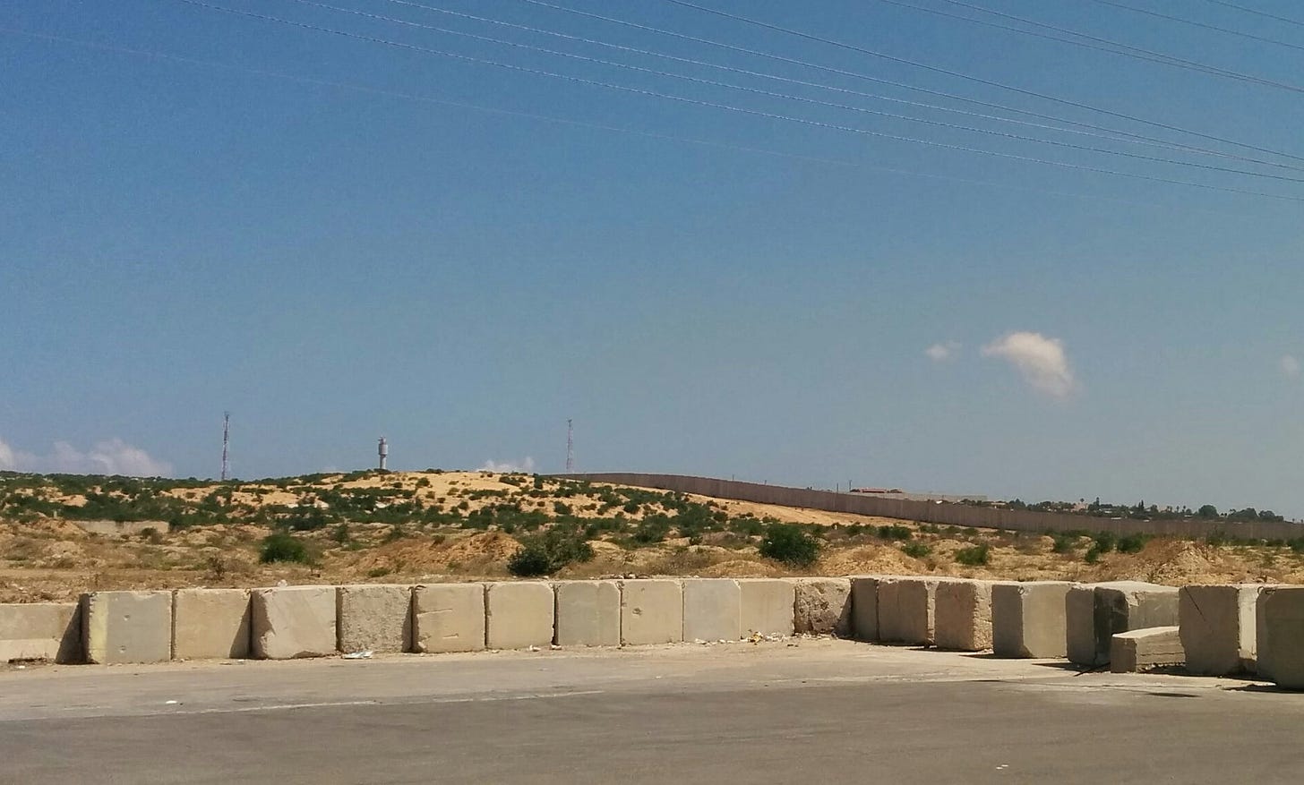 A long concrete wall with a guard tower extended above it below a clear blue sky