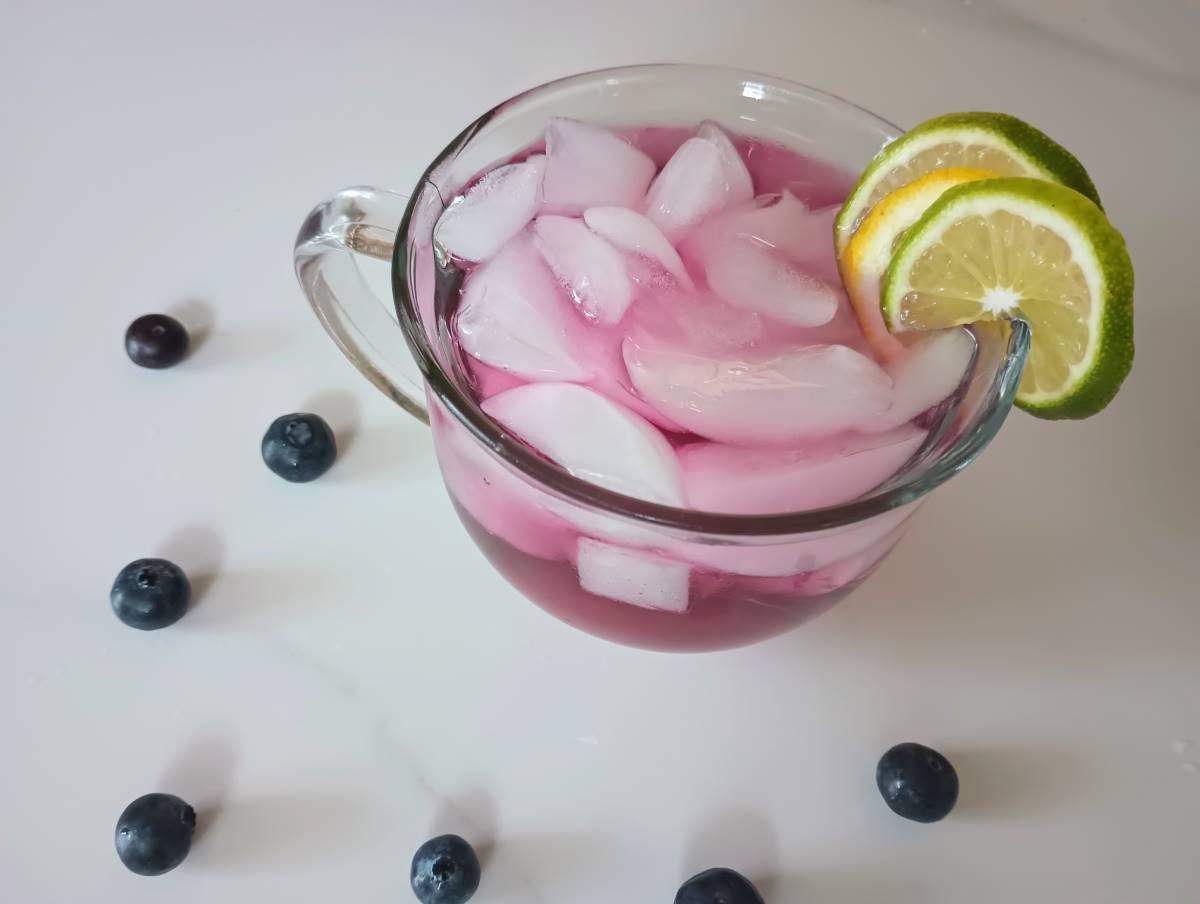 blueberry lavender iced tea mocktail in glass mug with lime and lemon slices.