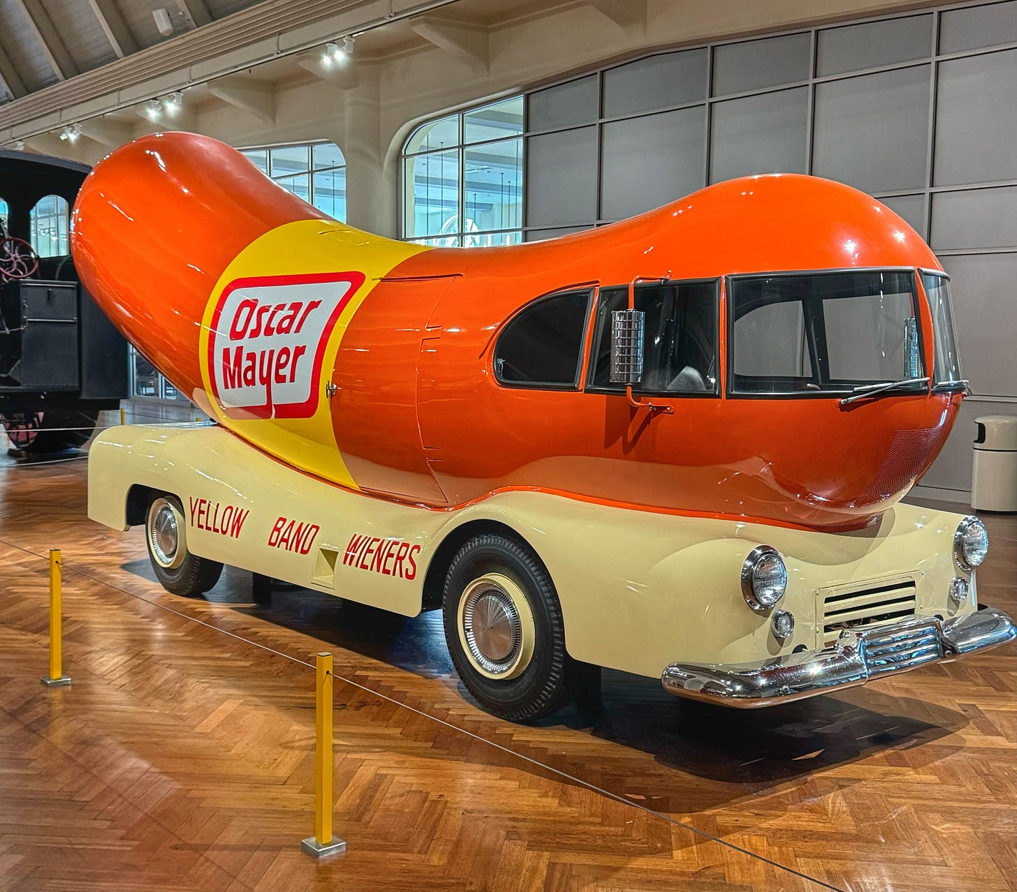 The Oscar Mayer Wienermobile, a vintage sedan that has had a large sausage cabin added to it, on display at the Henry Ford Museum. Its side reads "Yellow Band Wieners"