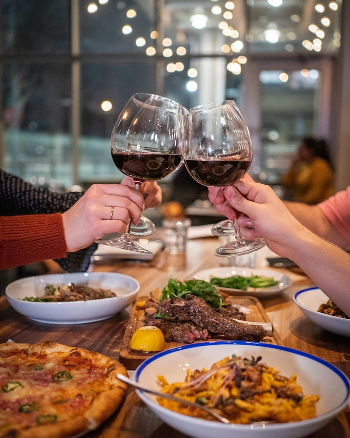 People with wine-glasses at table filled with food.