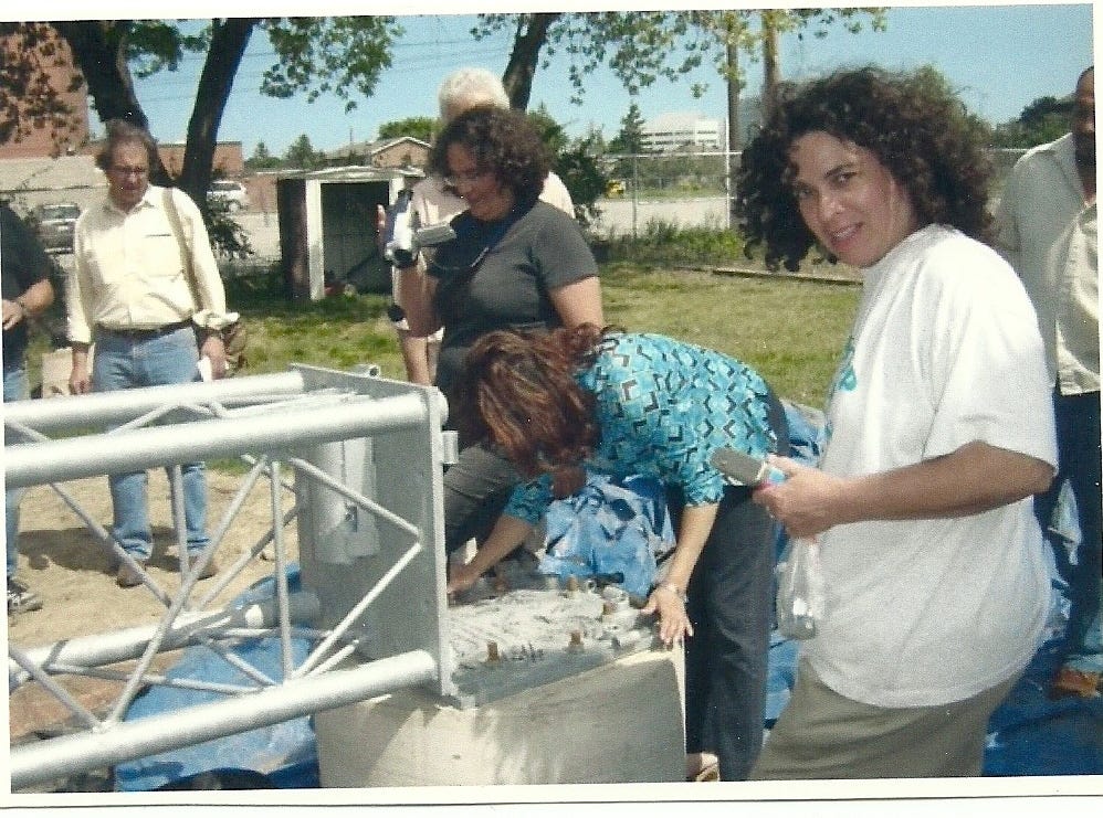 A woman signs the base of the radio broadcasting tour for CHHA 1610 AM circa 2004. Other people look on and look at the camera.