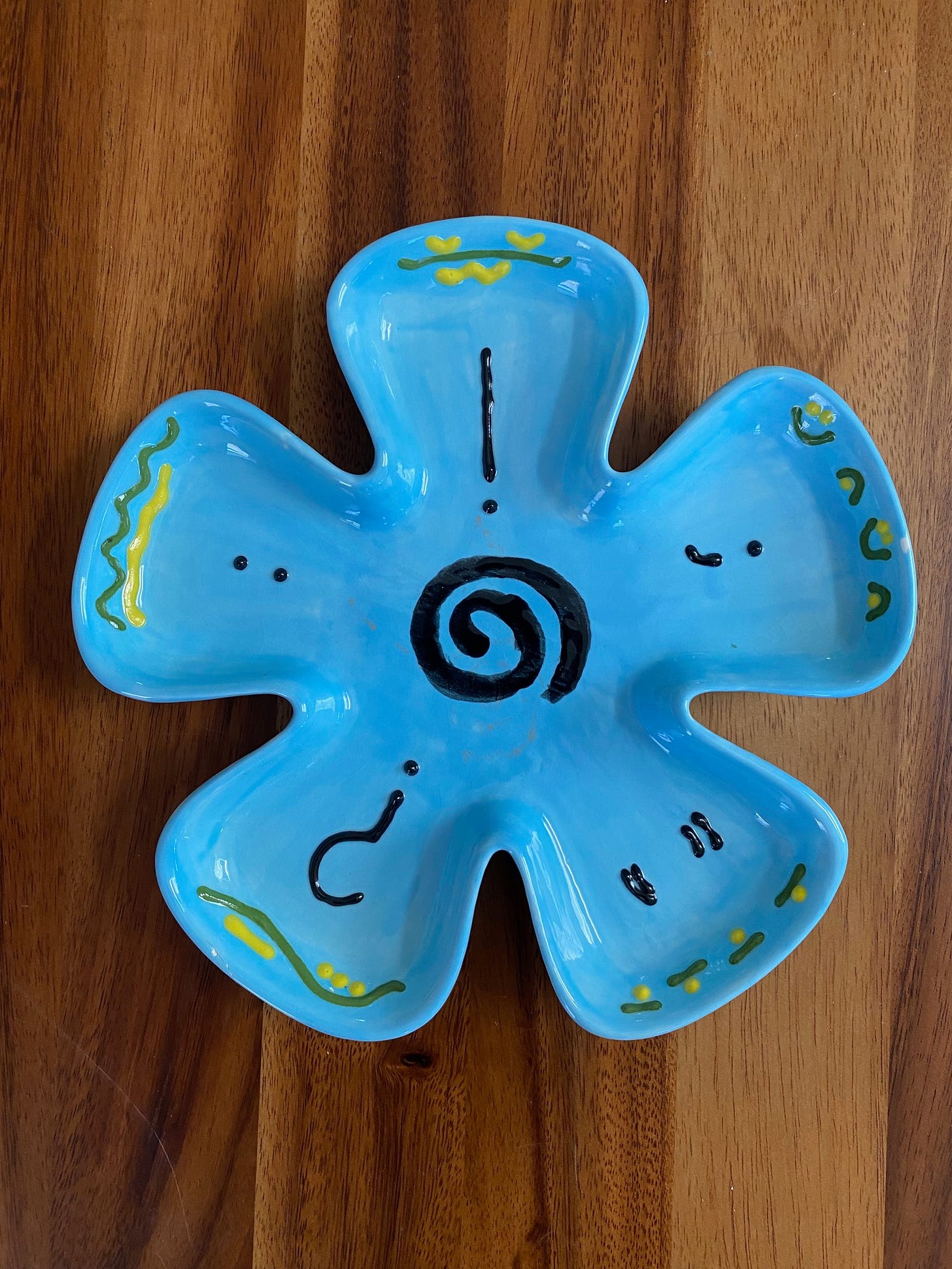 Blue ceramic dish in shape of flower with punctuation symbols and squigglies in green, yellow, and black.